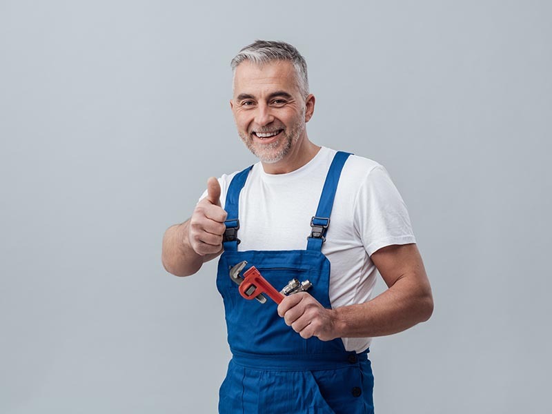 Cheerful repairman and plumber giving a thumbs up, he is smiling and holding an adjustable wrench